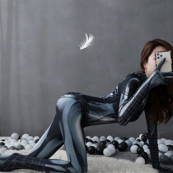 Woman in black spider-man bodysuit posing with phone, surrounded by balls and a floating feather.