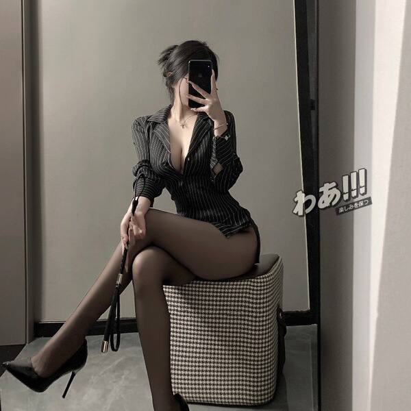 Woman in striped sexy secretary outfit with black stockings and heels, posing seductively on checkered stool.