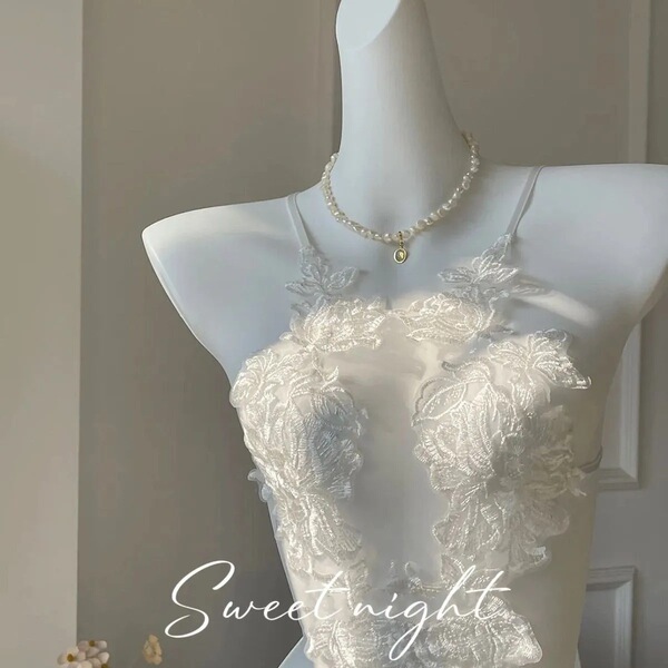 White sheer lace bodysuit with floral embroidery and pearl necklace on mannequin.