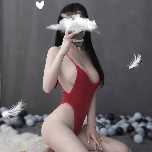 A woman poses with a red swimsuit featuring an open-crotch design, set against a gray background with feathers floating nearb...