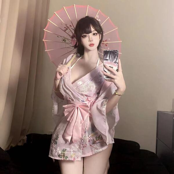 A person wearing a pink floral yukata robe with satin trim, bow detail, and embroidery, holding an umbrella while taking a se...