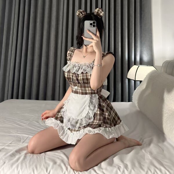 A person wearing a plaid maid costume dress with lace details and bunny ears, sitting on a bed while taking a selfie. perfect...