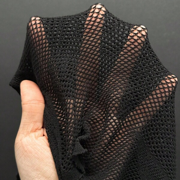A hand holds a black twill lace garment, showcasing its intricate mesh design and delicate texture. the piece features a shee...