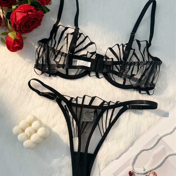 Sheer black lace lingerie set with delicate straps, styled with red roses and pearls for a sensual, romantic look.