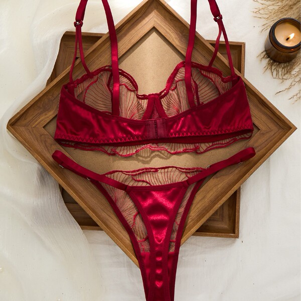 Wine red plus size lingerie set featuring a sheer mesh bra and panty with lace cutouts, displayed on a wooden tray.