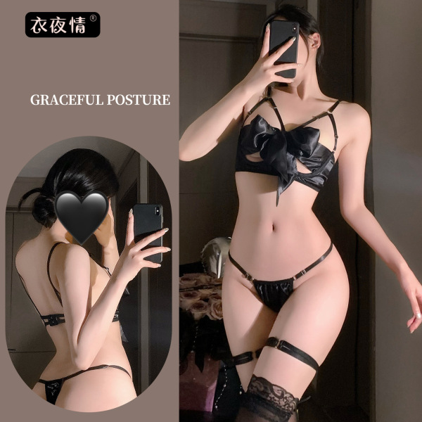 Woman modeling black lace bralette and thong set with bow-tie detail, sheer straps, and garter belts in elegant pose.