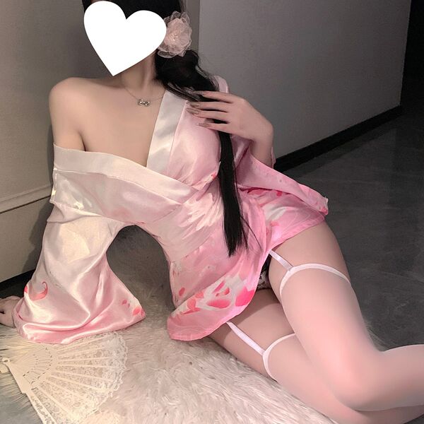 A woman poses in a pink satin kimono-style outfit with floral designs, featuring a deep v neckline and thigh-high stockings, ...