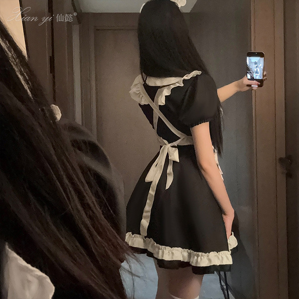 A woman wearing a black maid costume with white accents, taking a mirror selfie. the outfit features puffed sleeves and a tie...