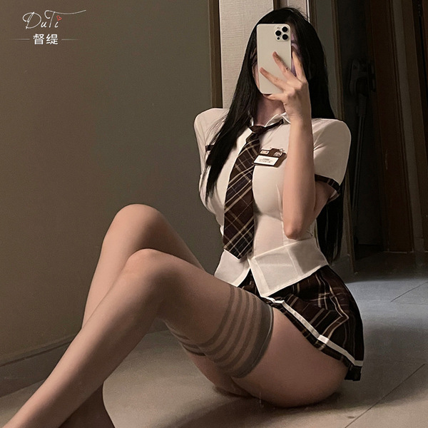 A woman poses with a smartphone, wearing a white blouse, brown tie, and plaid skirt, embodying a seductive student uniform st...