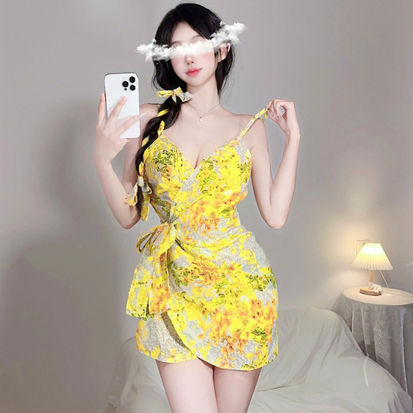 A woman poses with a phone, wearing a yellow floral lace bodysuit set. the outfit features spaghetti straps and a tie-front d...