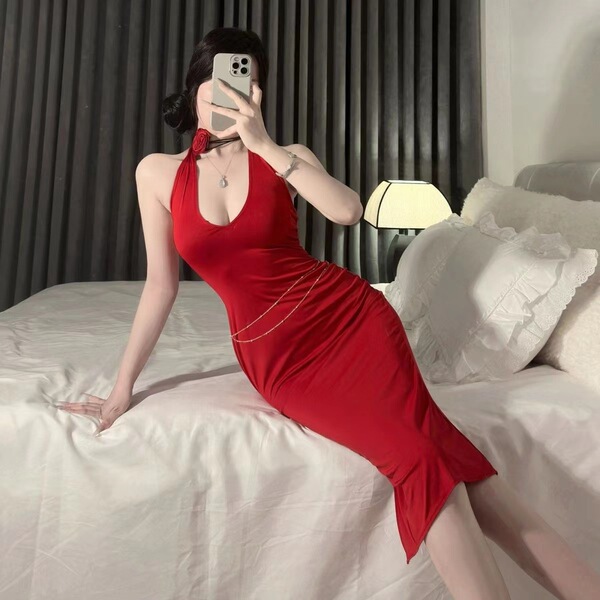 A woman poses on a bed wearing a striking red yilanfang new bride cheongsam lingerie dress, featuring a deep v-neck halter de...