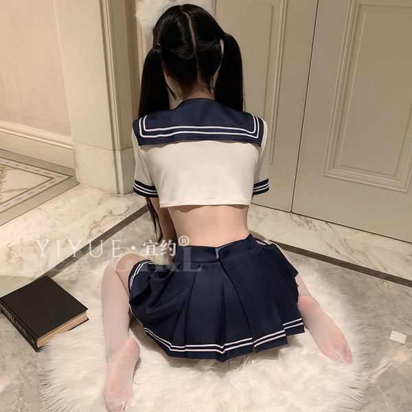 A girl wearing a navy blue and white sailor-style school uniform sits on a fluffy rug indoors, with a book beside her. the ou...