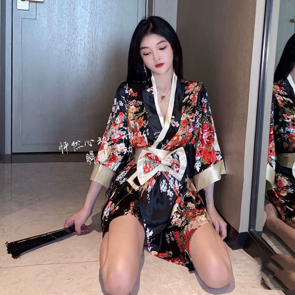 A woman wearing a floral-patterned japanese-style robe, featuring a low-cut design and bow tie, sitting on the floor with a w...