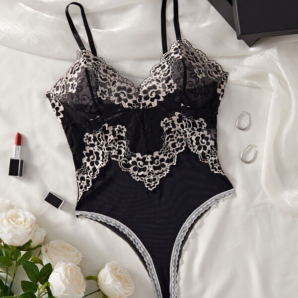 Black lace mesh bodysuit with floral detailing, displayed on white silk with roses and accessories.