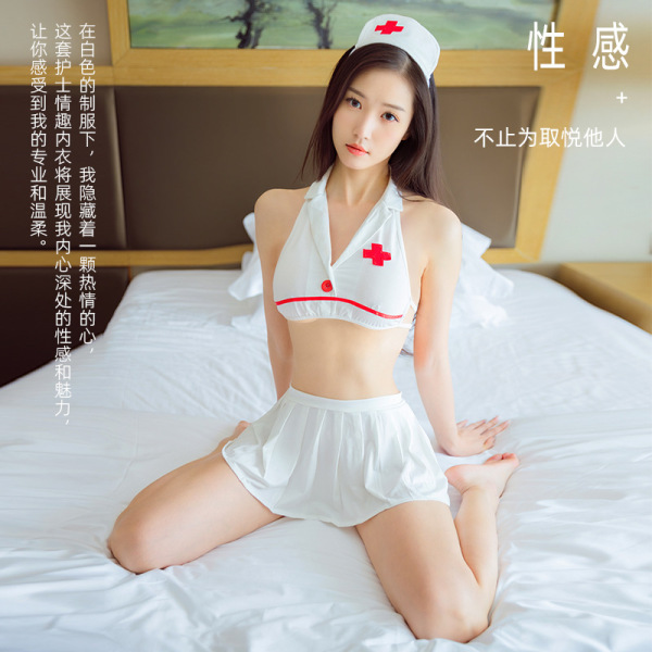 Woman wearing white nurse costume lingerie set with red cross details, sitting on bed in sexy sleepwear role play outfit.