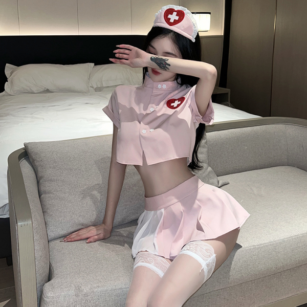 Woman in pink nurse-themed lingerie set with crop top, skirt, and lace stockings on a couch.