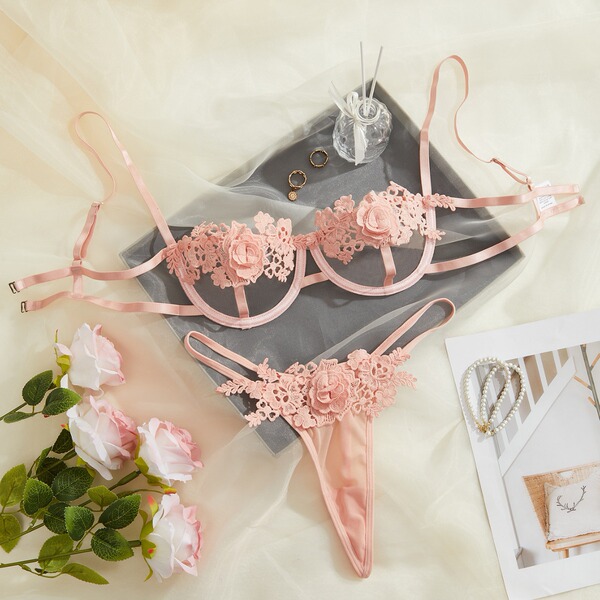 Pink lace lingerie set with floral details, displayed on a soft background with roses and accessories.