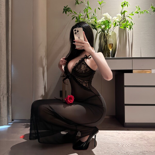 Woman in black sheer nightsigh nightseduce lingerie set with lace, posing with rose and phone.