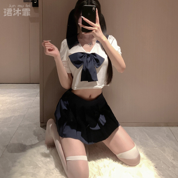 A person wearing a japanese-style school uniform, featuring a white crop top with a navy bow and pleated skirt, paired with s...