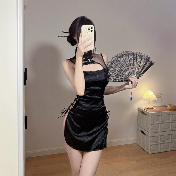 Woman in black sheer cheongsam lingerie set holding a lace fan, posing in a softly lit room.