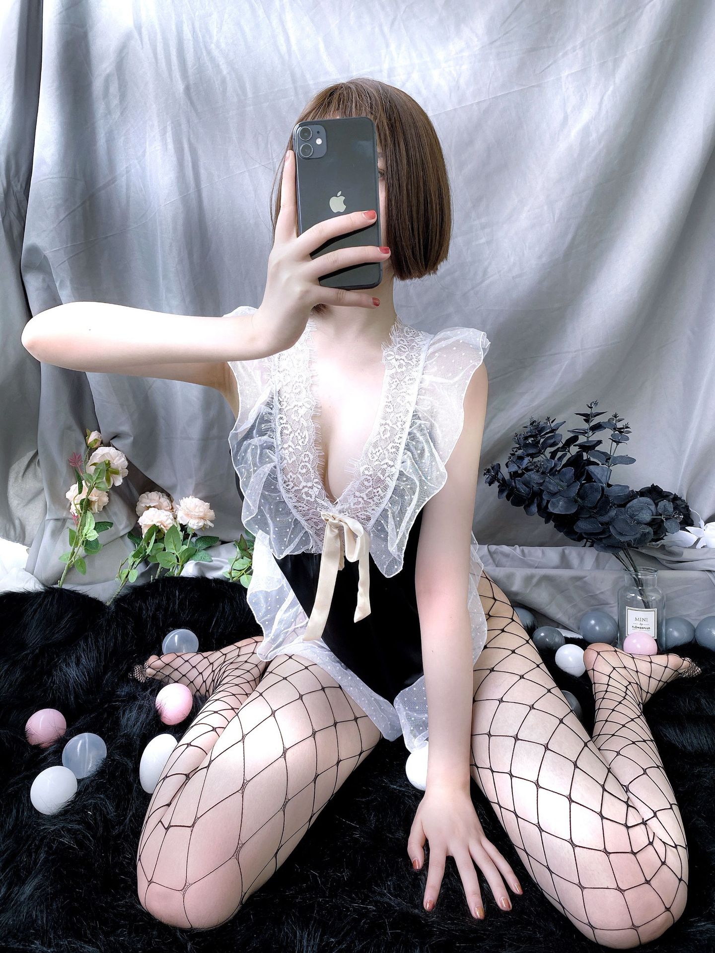 A woman poses with a smartphone, wearing a black lace lingerie set featuring fishnet stockings. the outfit includes a sheer t...