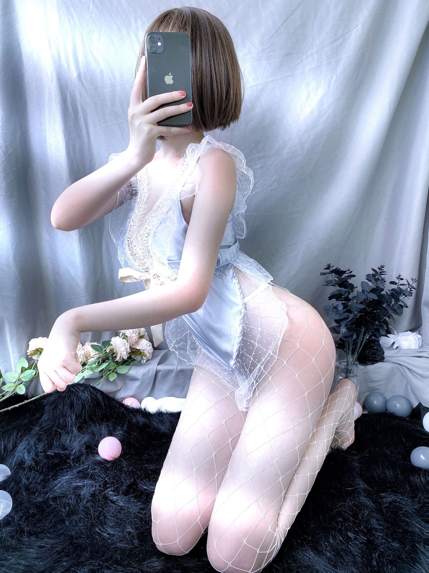 A woman poses with a smartphone, wearing a delicate lace lingerie set paired with fishnet stockings. the outfit features shee...