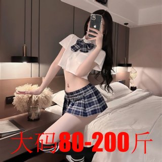 Woman modeling plus size jk uniform set with white crop top, blue plaid bow tie, and pleated mini skirt in bedroom.