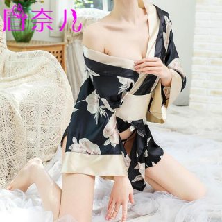 A woman wearing a black floral print robe with beige accents, tied at the waist, sitting on a white surface. the design featu...