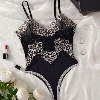 Black lace mesh bodysuit with floral details, styled as sensual sleepwear lingerie for women, displayed on white silk with ro...