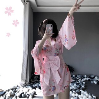 A woman poses with a phone, wearing a pink floral japanese-style kimono robe set featuring lace details and a bow belt. the e...