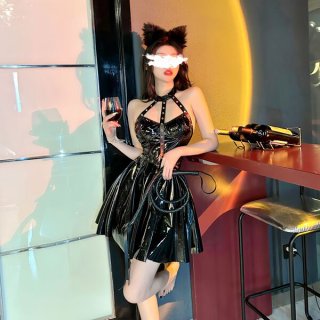 Woman in shiny black pvc catwoman costume with lace-up bodysuit, garter belt, and thong, holding wine glass and whip.