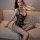 Woman wearing qingyeguo black lace bodysuit with sheer mesh and open-crotch stockings, seated on beige sofa.