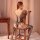 Woman wearing qingyege plus size black mesh bodysuit with sheer open-crotch design and attached stockings, seated on wooden c...