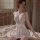 Woman wearing white lace sleep dress with push-up cami top and elegant trim, sitting on bed in soft lighting.