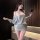 Woman wearing chaomu sensual lingerie dress, one-shoulder backless cutout bodycon mini dress in soft gray, posing with phone.