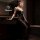Woman in black seductive no-remove bodysuit with gold floral details, posing in a dimly lit bathroom.
