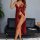 Woman wearing red sheer lace sleep dress with matching lingerie, posing elegantly beside black leather sofa in modern room se...