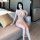 A woman poses elegantly on a couch wearing a sheer pink lace nightgown, featuring deep v-neckline and adjustable straps, perf...
