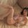 Woman wearing pink cat costume lingerie with fishnet stockings and bow details on bed.