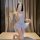 Woman wearing white lace bodysuit with tie-neck and open-crotch design, posing on bed in soft lighting.