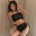 Woman modeling black devil-themed lingerie set with red heart details, open-bust top, lace shorts, and horn headband.