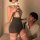 Woman in a seductive lace bodycon dress with thigh-high stockings, capturing a mirror selfie in a cozy room.