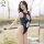 A woman poses confidently wearing a navy blue one-piece swimsuit with deep cutouts and high slits, featuring a glossy finish....