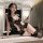 Woman modeling black lace plus size lingerie set with sheer panels and garter straps, holding a riding crop in elegant bedroo...