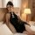 Woman lounging on bed in black off-shoulder cheongsam dress with white frog buttons and body-con wrap skirt.