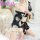 A woman wearing a black floral print robe with beige accents, tied at the waist, sitting on a white surface. the design featu...