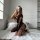 A woman poses on a white rug, wearing a black sheer bodysuit with cutouts and lace mesh design, perfect for nightclub wear or...