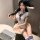 Woman in white student-themed cosplay lingerie set with blue accents, seated at desk with laptop.