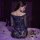Woman wearing a blue lace bodycon skirt set with sheer sleeves, seated on a bed with rose petals for date night.