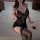 Woman wearing black lace sleepwear set with deep v-neck bodysuit and elastic straps, seated on bed with rose petals.